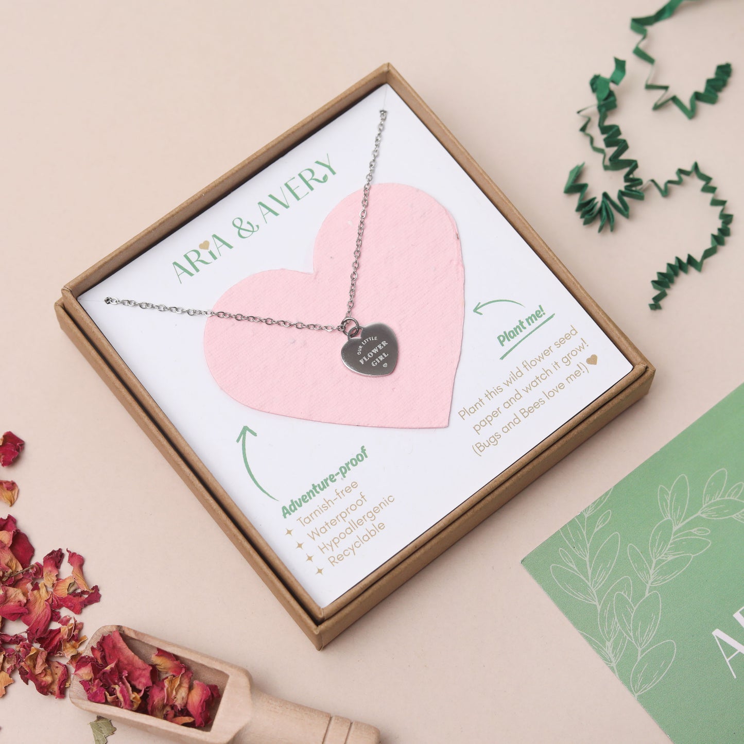 A heart-shaped pendant necklace presented in a gift box with a plantable seed paper heart. The necklace has a silver chain and a silver heart pendant engraved with 'OUR LITTLE FLOWER GIRL'.